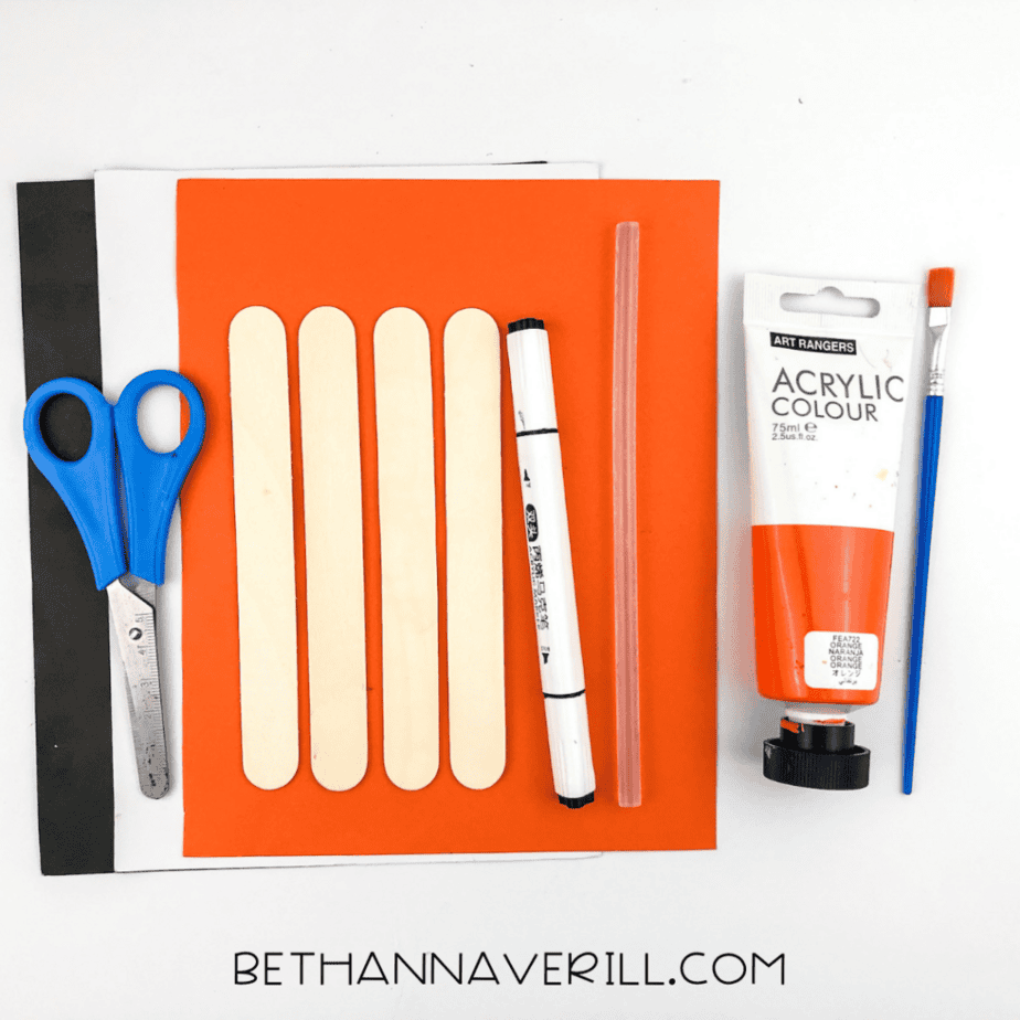 Craft supplies for a fox popsicle stick craft including wooden craft sticks, orange acrylic paint, paintbrush, scissors, cardstock, marker, and glue stick on a white background.