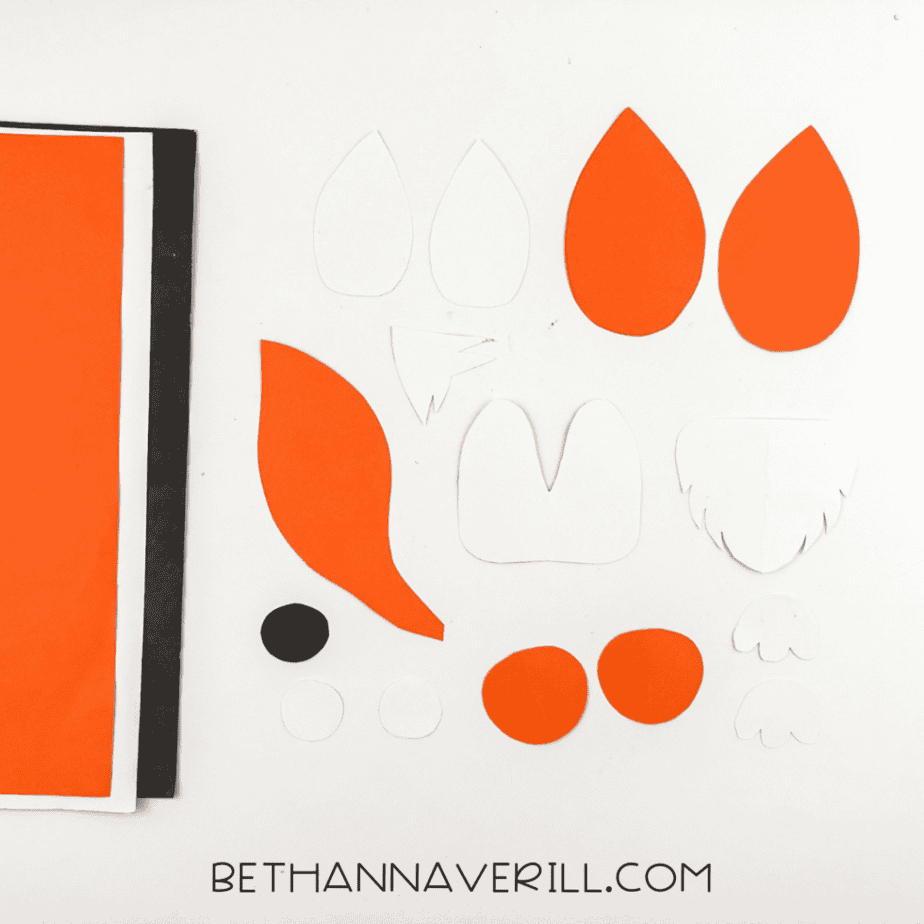 Orange and white paper pieces cut for a fox popsicle stick craft including ears, tail, paws, and facial shapes.