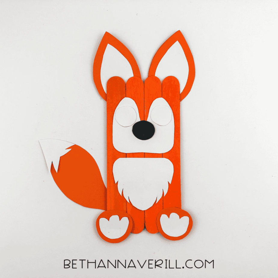 Fox popsicle stick craft with face pieces added including white muzzle and black nose.