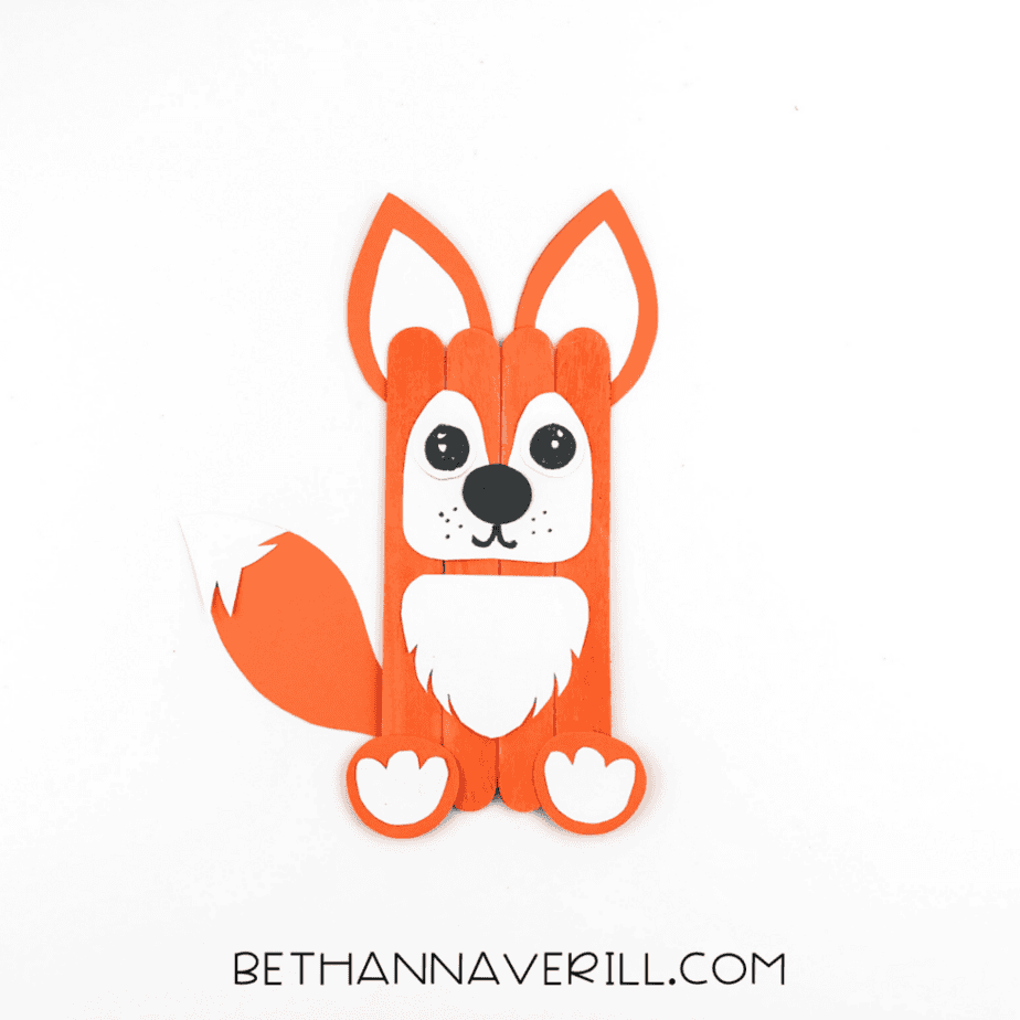 Completed fox popsicle stick craft with drawn facial details including eyes, whisker dots, and mouth.