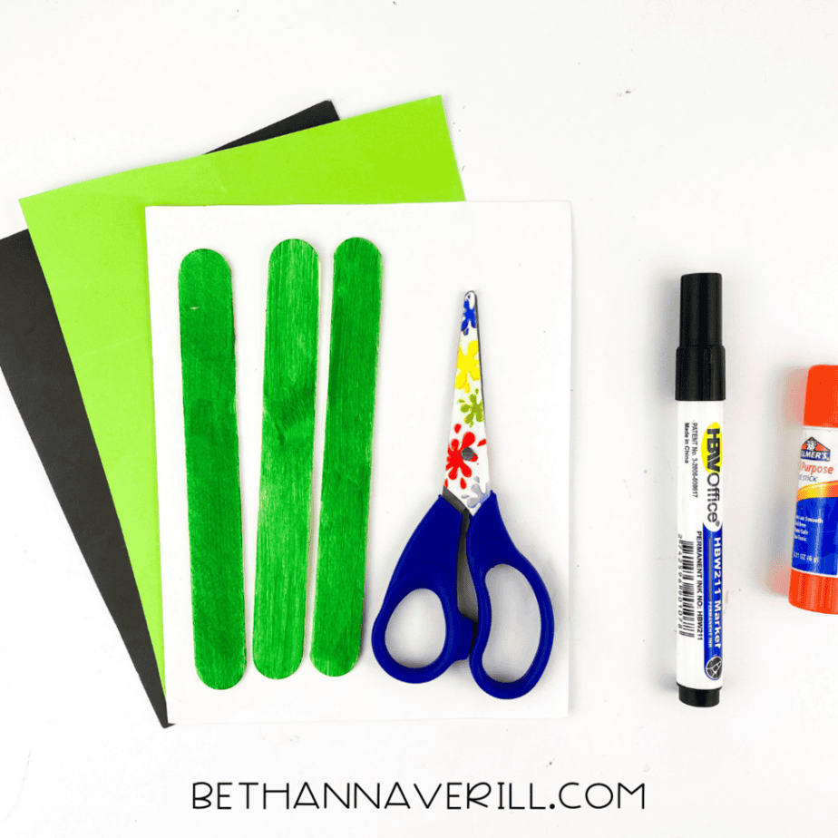 Craft supplies for a Frankenstein popsicle stick craft including green painted craft sticks, green and black cardstock, scissors, glue stick, and marker.