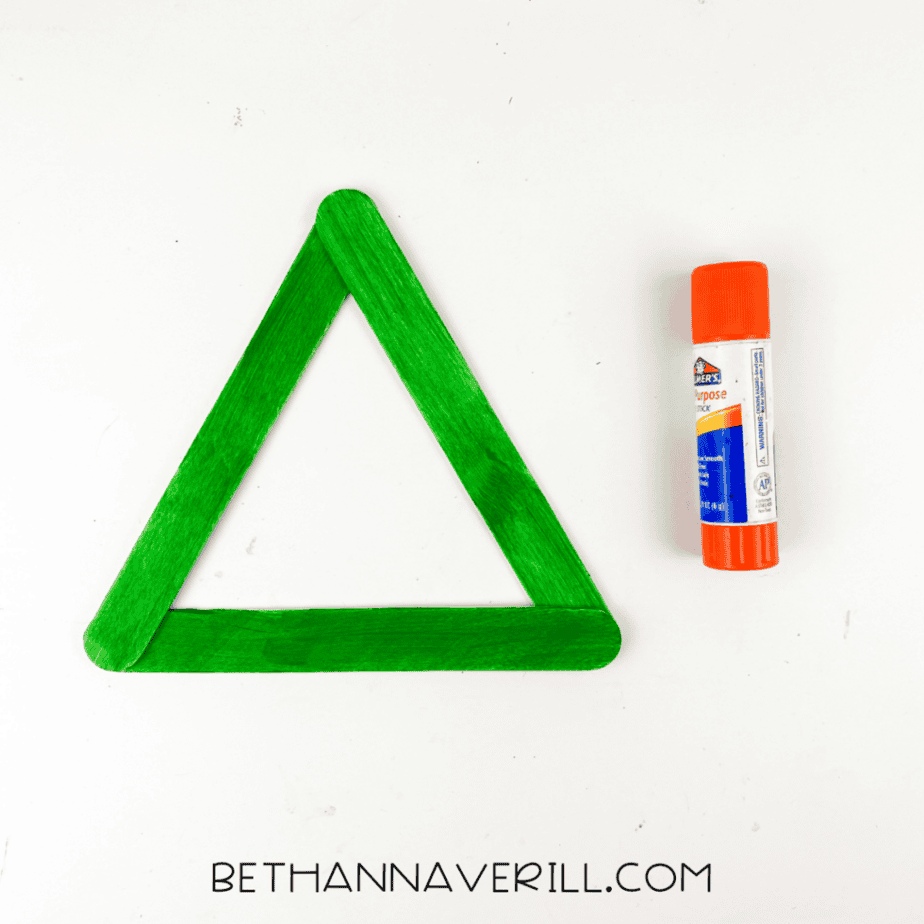 Three green painted popsicle sticks glued together in a triangle shape to form the base for a Frankenstein popsicle stick craft.