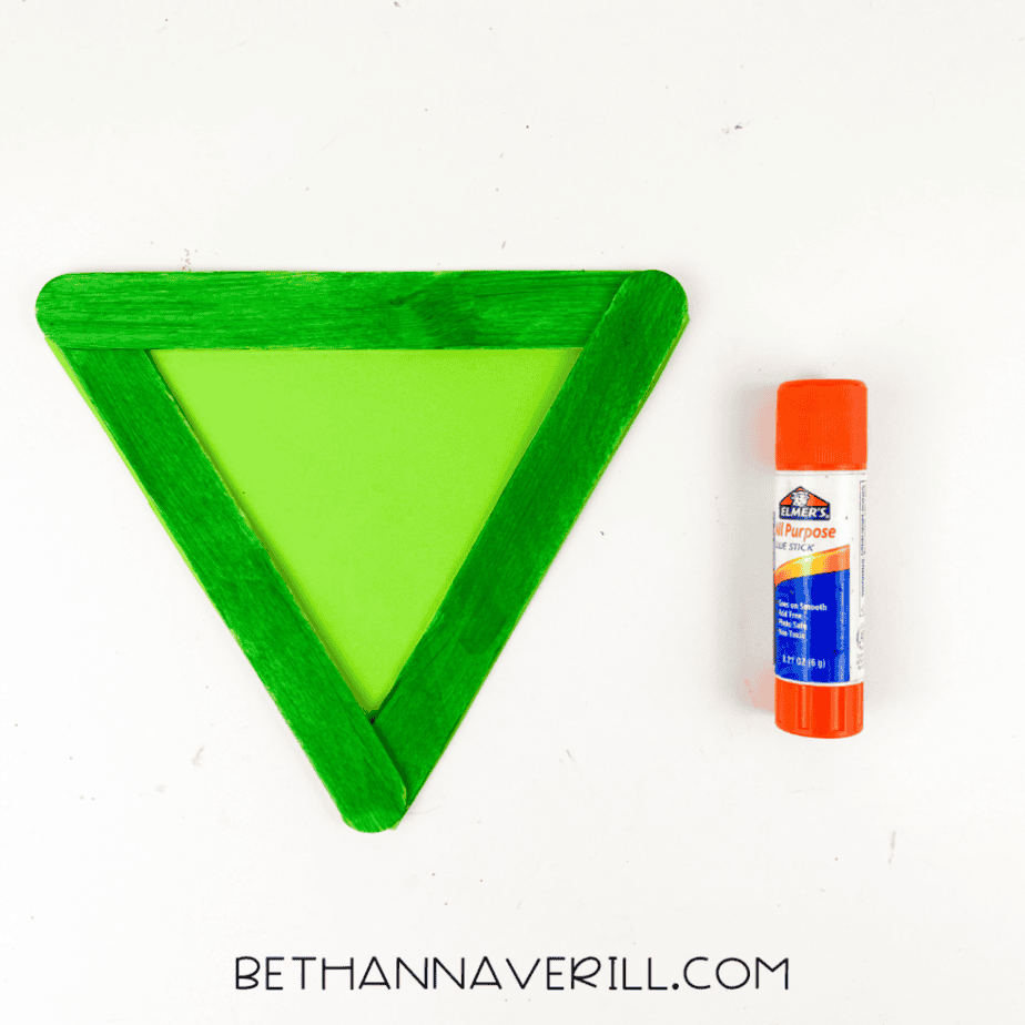 Green paper triangle glued inside a popsicle stick frame forming the base of a Frankenstein craft.