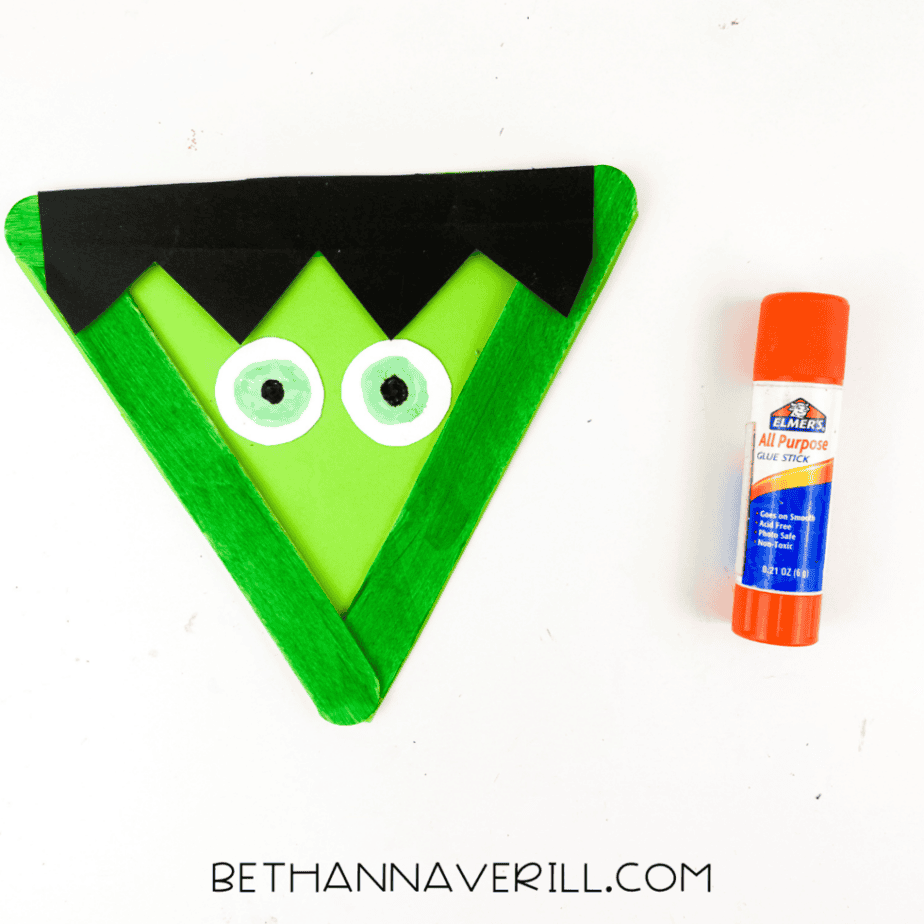 Frankenstein popsicle stick craft with black paper hair and paper eyes added to the green face.