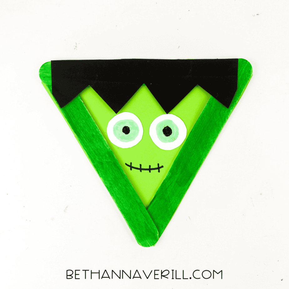 Finished Frankenstein popsicle stick craft with green face, black hair, and drawn stitched smile.