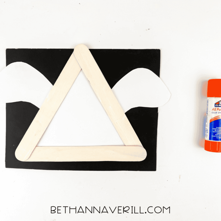 Paper ghost arms attached behind a triangle popsicle stick frame during assembly of a ghost craft.
