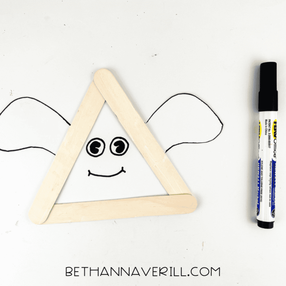 Ghost popsicle stick craft with eyes and a smile drawn on the white triangle face using a black marker.