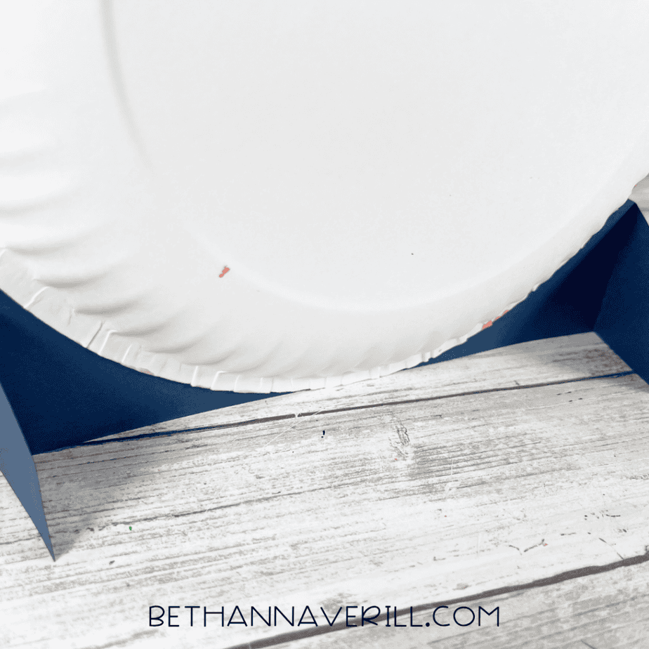 Close-up of the back of a white paper plate attached to a folded dark blue paper base.