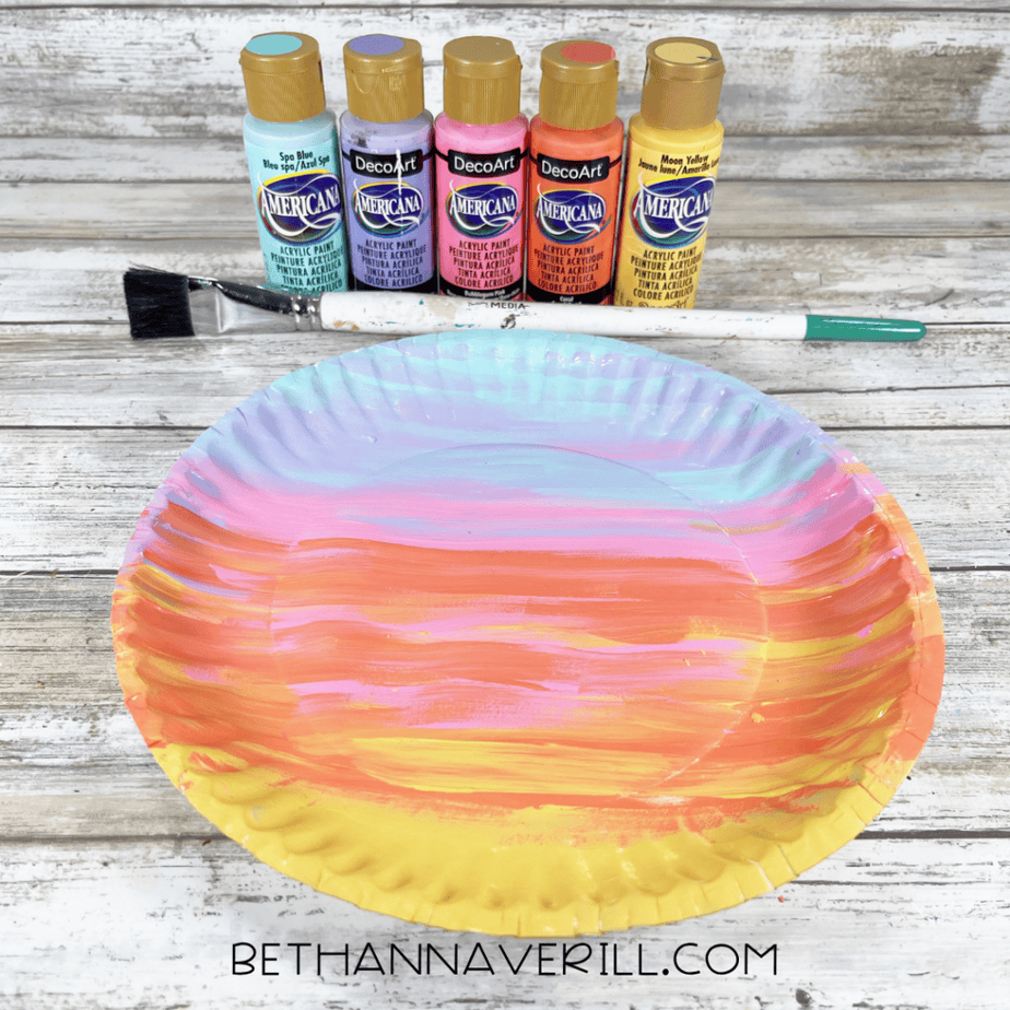 Paper plate painted in blended pastel stripes of pink, purple, blue, orange, and yellow.