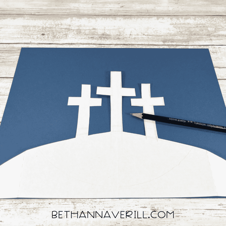 White template of three crosses on a hill drawn on dark blue paper with a pencil.