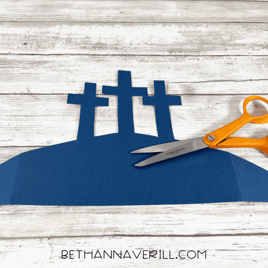 Dark blue paper cut into a hill shape with three cross silhouettes, scissors nearby.