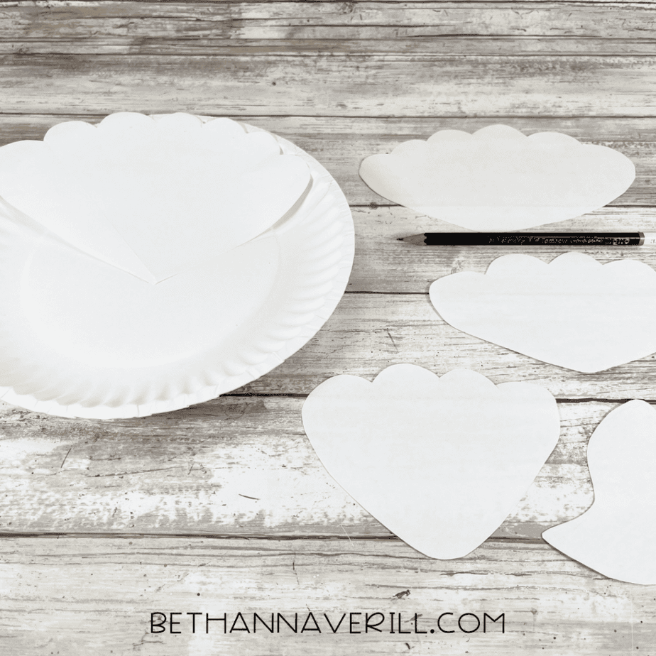 Paper plate with scallop shapes traced on it and paper templates for cutting mermaid tail pieces.