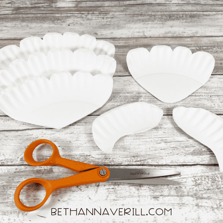 Several scalloped paper plate pieces cut out with scissors for a mermaid tail paper plate craft.