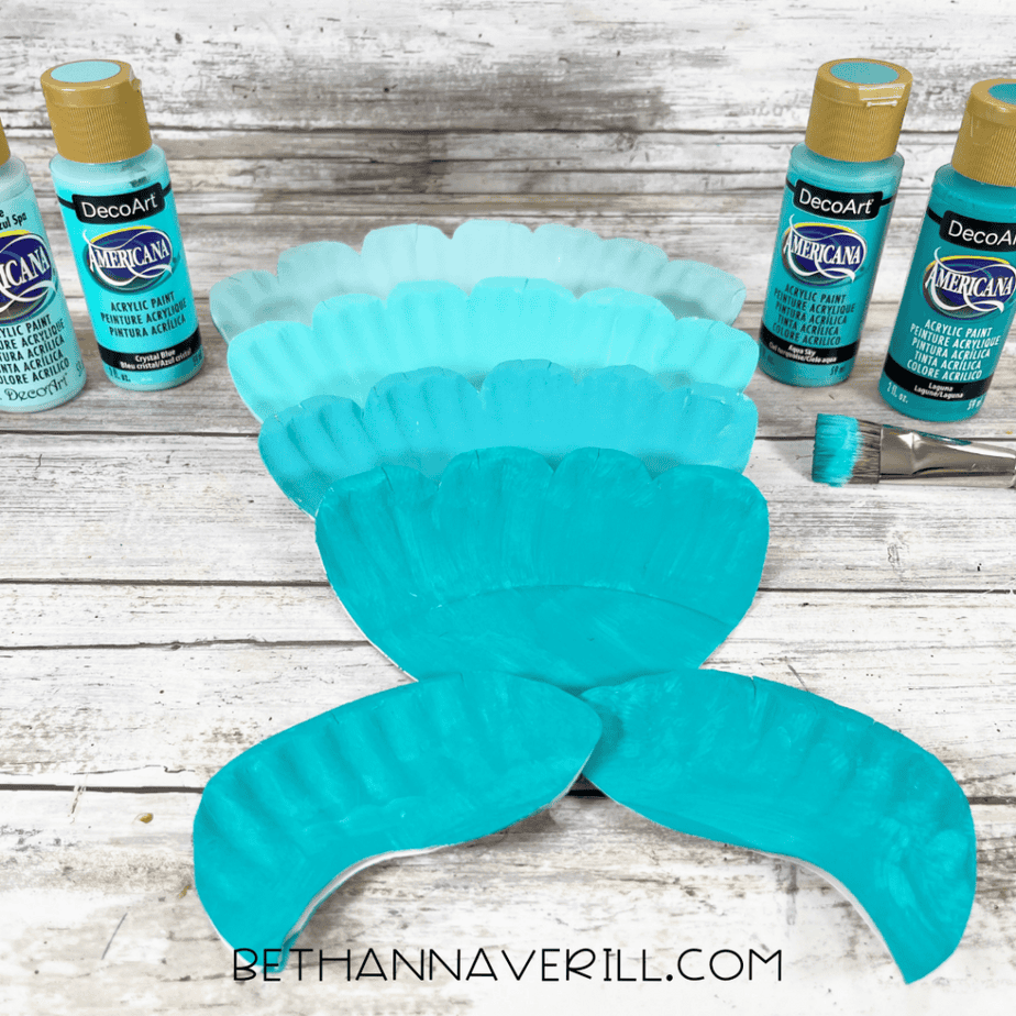 Paper plate pieces painted in shades of turquoise and aqua with acrylic paint for a mermaid tail craft.