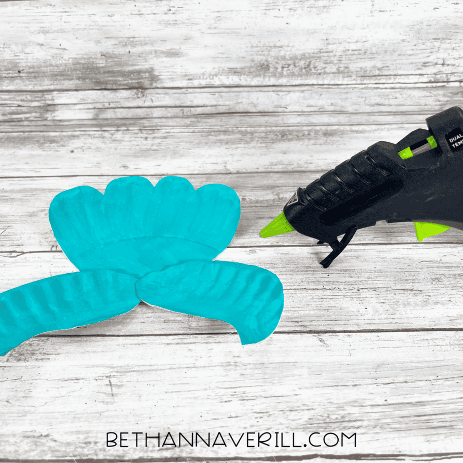 Painted paper plate tail fin pieces arranged together next to a hot glue gun.