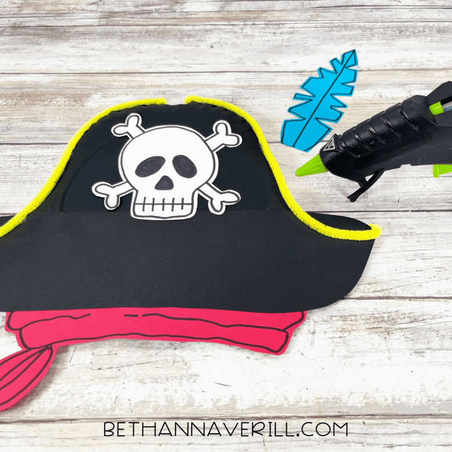 Adding skull emblem and feather decoration to pirate hat craft.