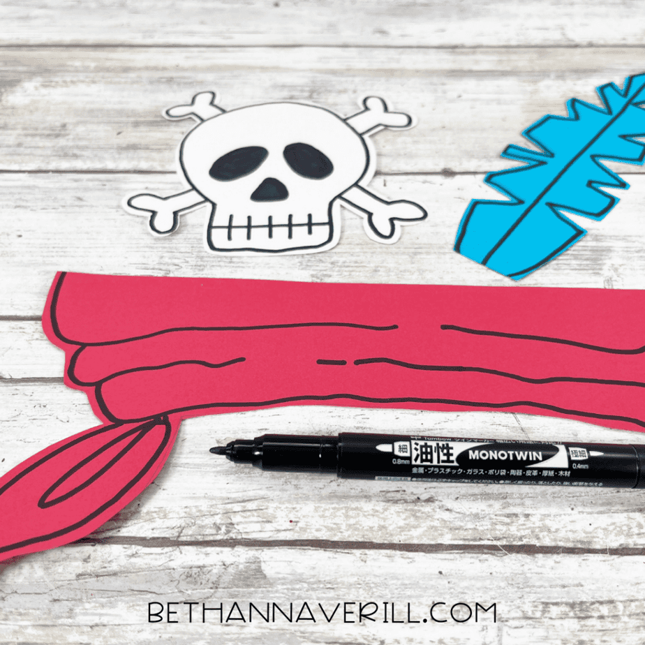 Adding details to red bandana piece with black marker for pirate hat craft.