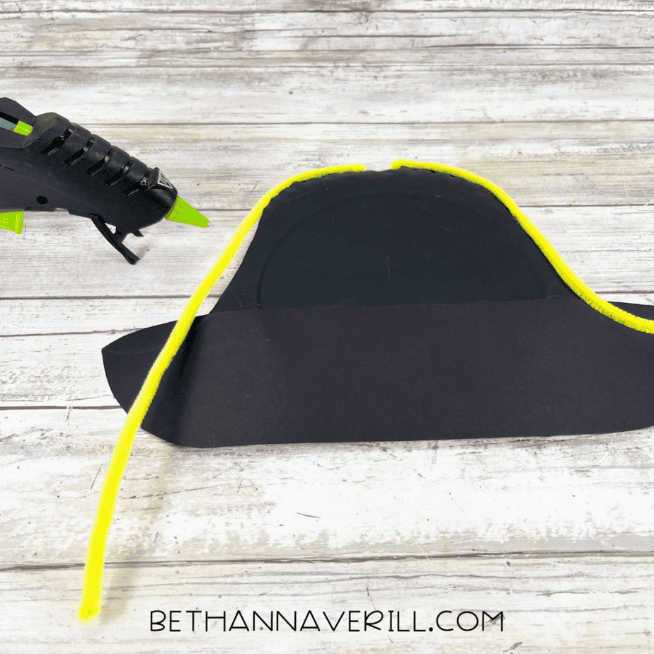 Gluing yellow pipe cleaner trim to edge of pirate hat.