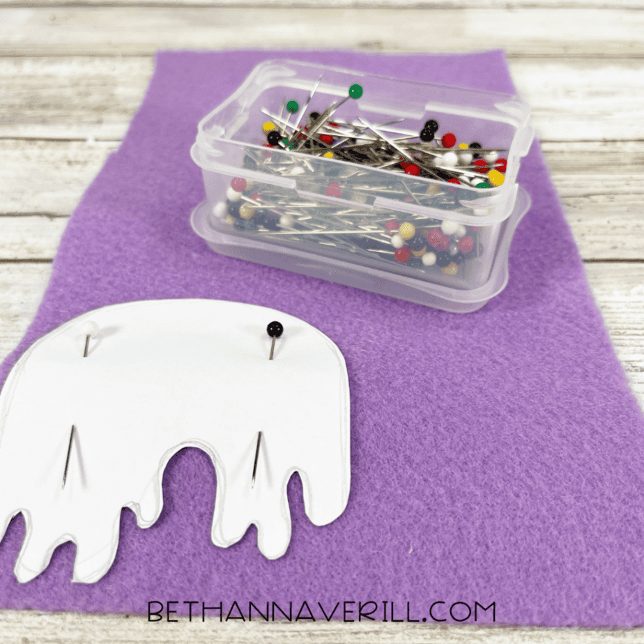 A piece of purple felt with a paper template pinned on top using straight pins.