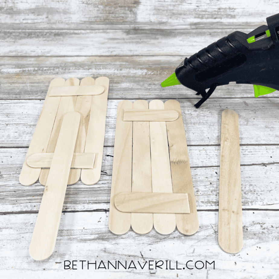 Two sets of craft sticks glued into rectangles, each reinforced with horizontal sticks on the back; a loose craft stick and glue gun beside them.