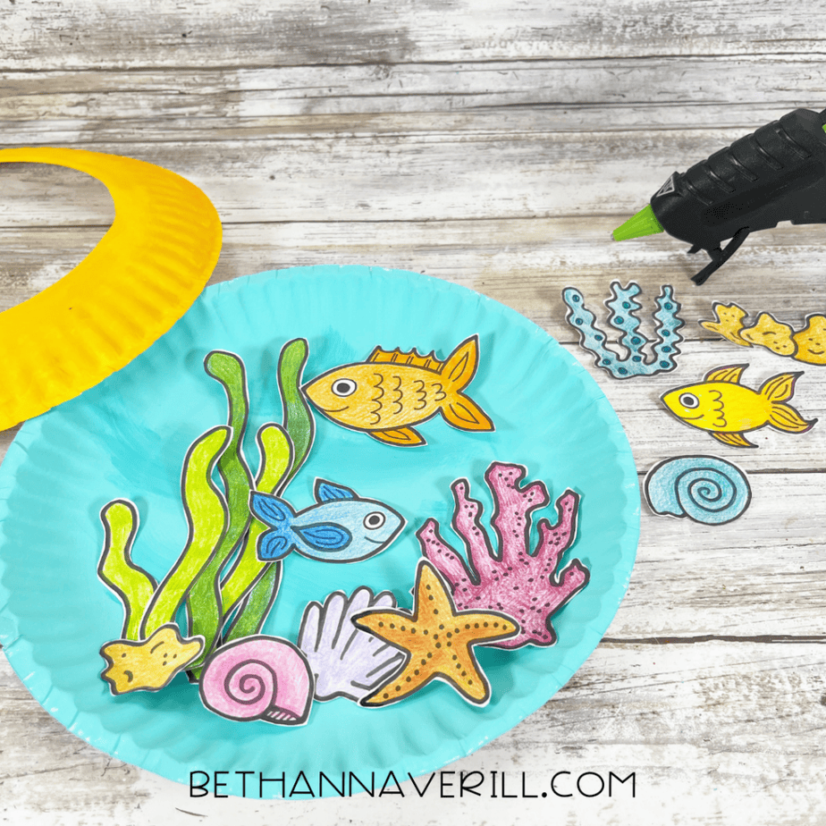 Blue plate with arranged ocean shapes inside and additional pieces off to the side, hot glue gun visible.