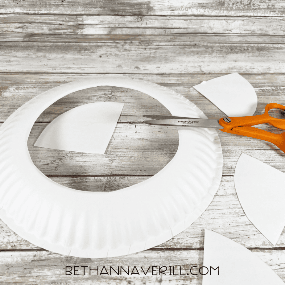 Paper plate with the center cut out, scissors beside it, and curved paper pieces removed.