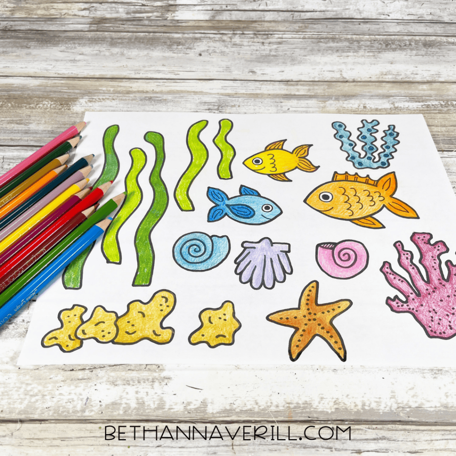 Colored version of the ocean-themed sheet with bright fish, seaweed, shells, and coral, with colored pencils to the side.