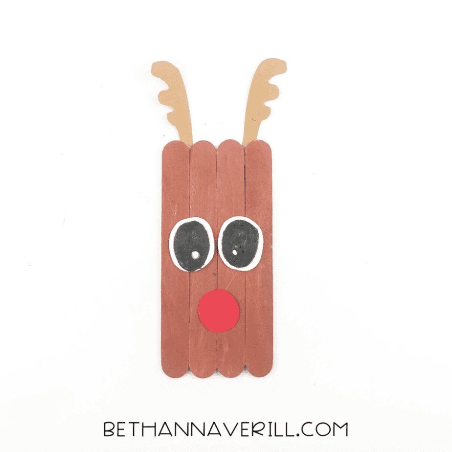 A completed reindeer popsicle stick craft with drawn black pupils and highlights inside the white paper eyes.