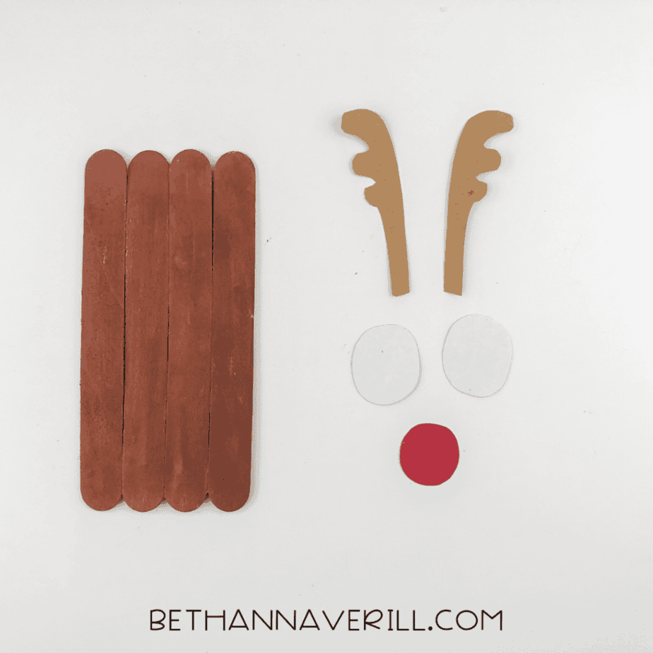 Four craft sticks painted brown with antler, eye, and nose cutouts arranged beside them.