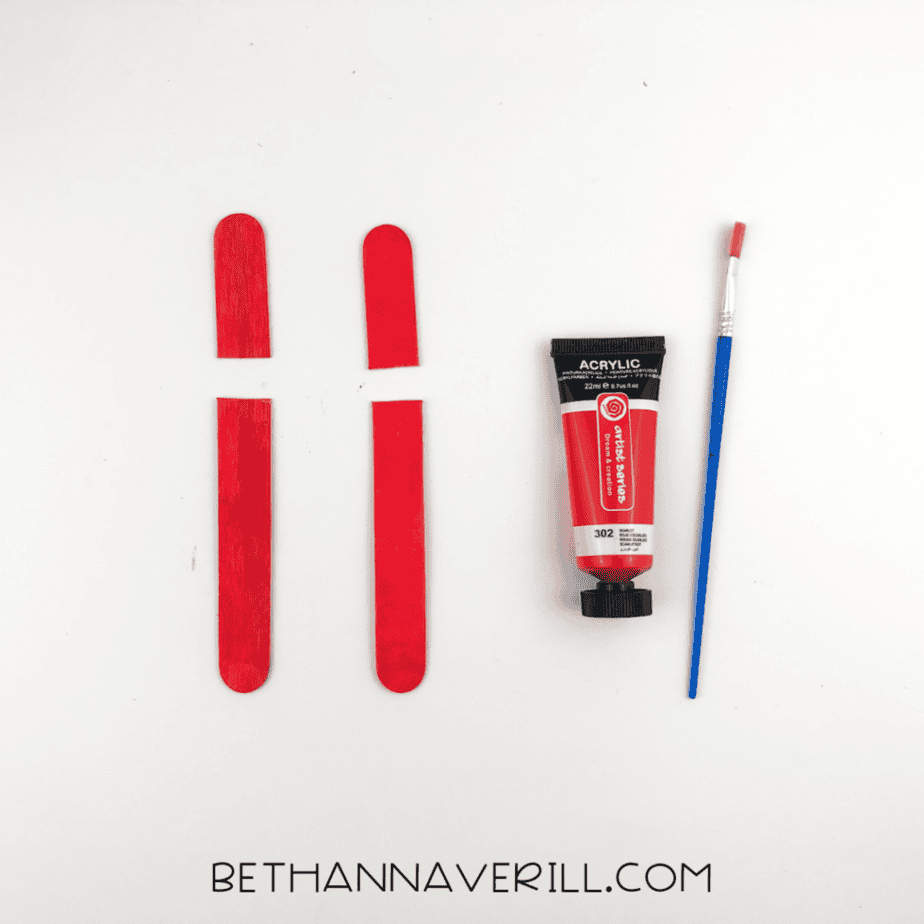 The popsicle sticks painted bright red and cut into shorter sections, arranged beside the paint and brush.