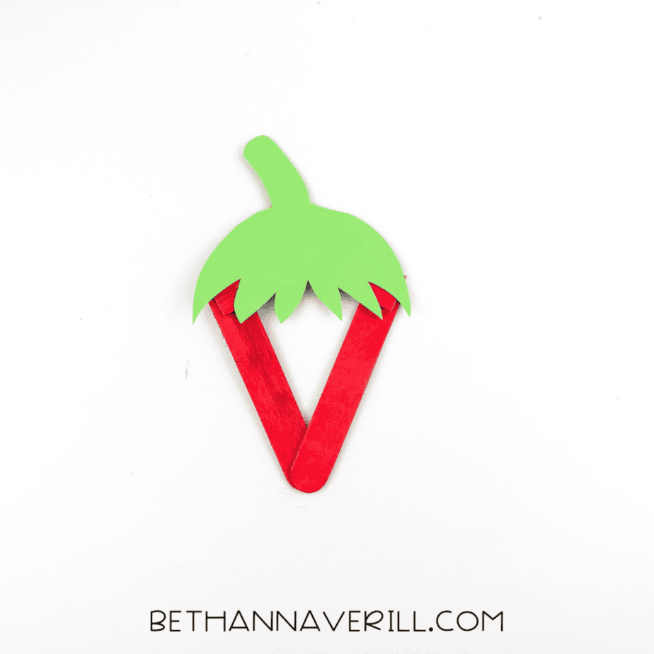 The green paper top attached to the red popsicle stick frame, forming a strawberry shape.