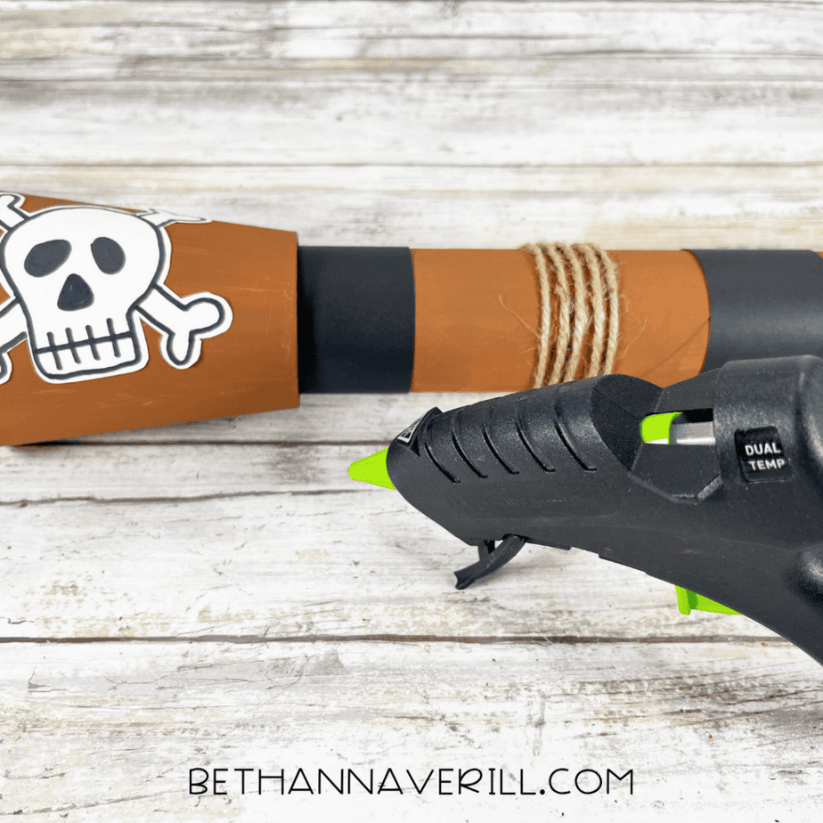 A close-up of the telescope showing the skull emblem, black bands, and twine wrapping while glue is applied.