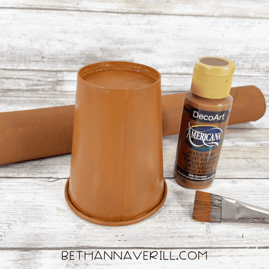 The paper cup and cardboard tube painted brown beside the paint bottle and brush.