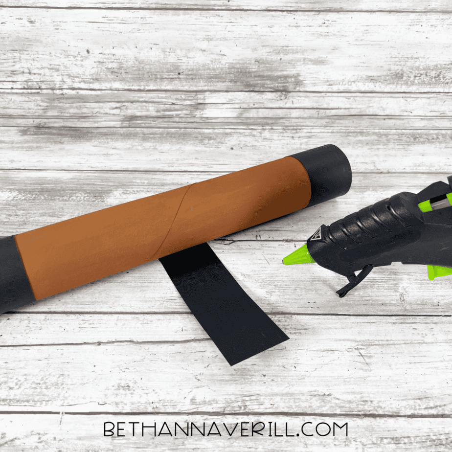 Black paper bands glued around both ends of the cardboard tube to create telescope accents.