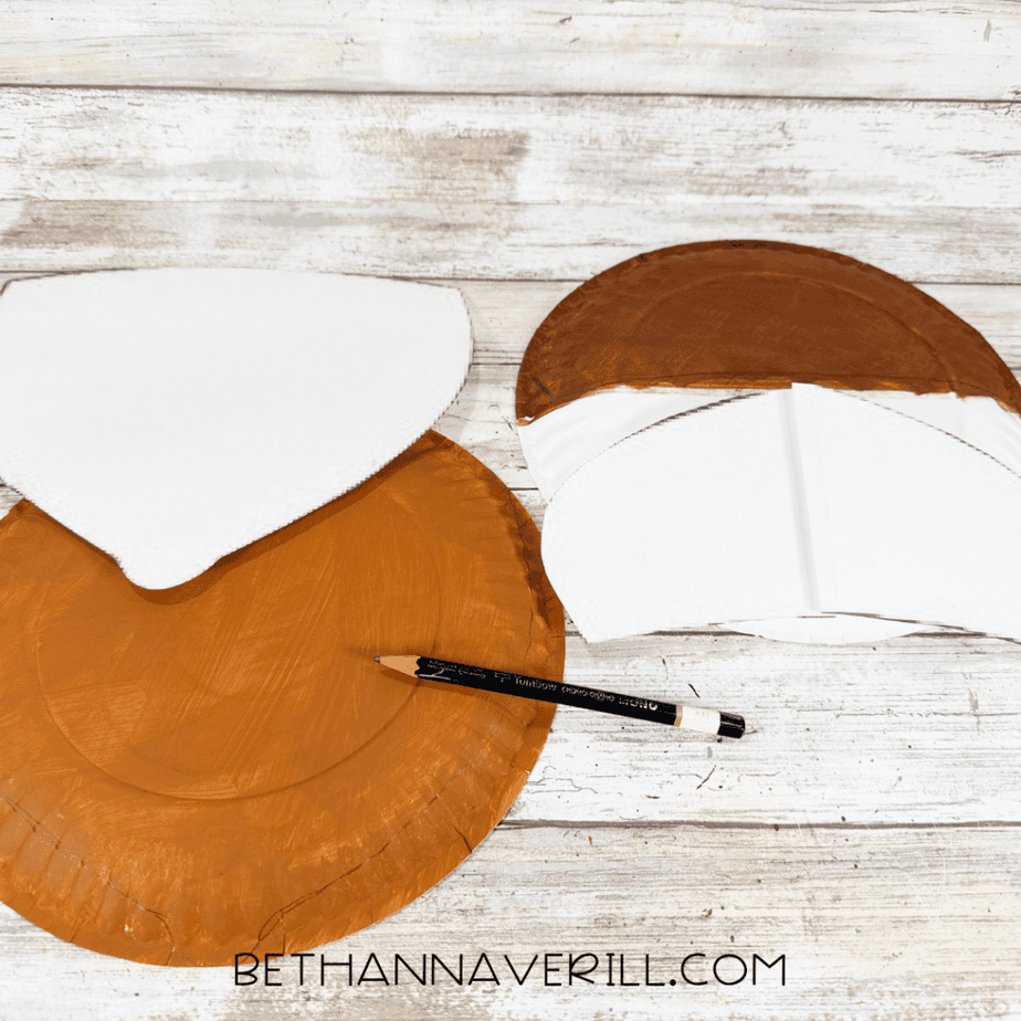 White paper templates placed over painted paper plates with a pencil nearby to outline the acorn craft shapes.