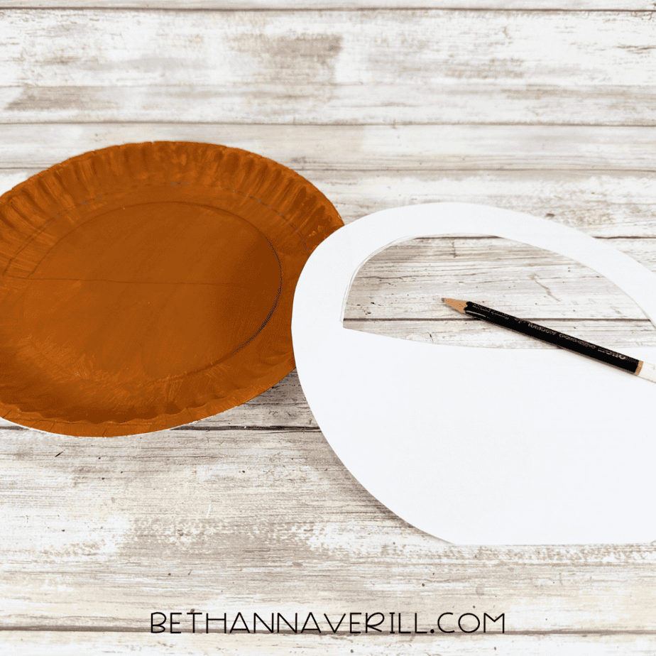 Brown painted paper plate with a semicircle traced onto it beside a white paper template and pencil.