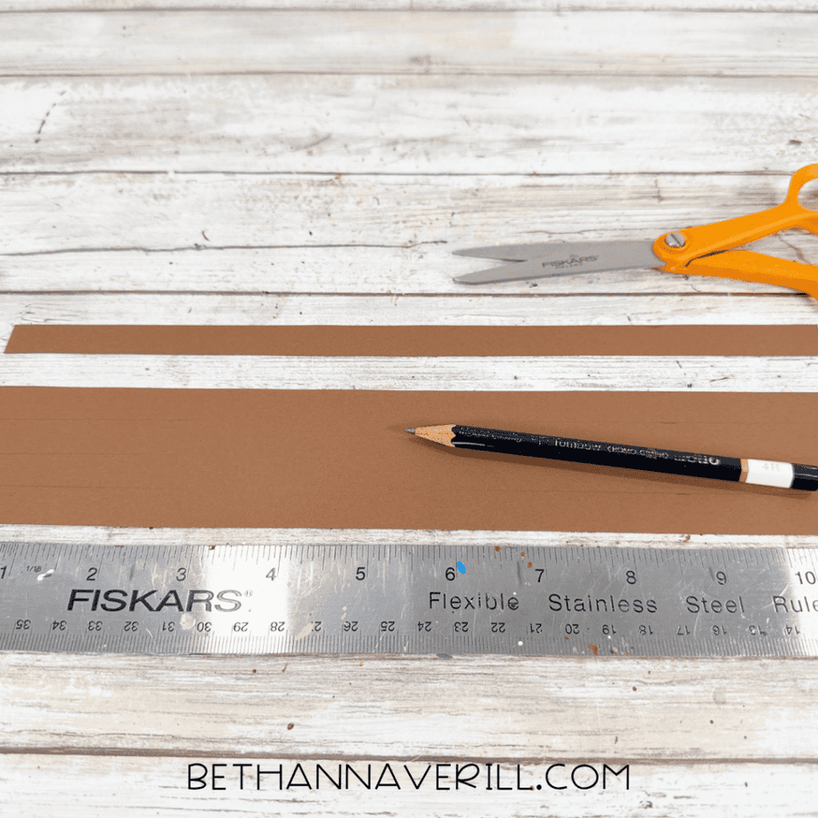 Brown construction paper strips measured and marked with a pencil and ruler for an apple basket craft.