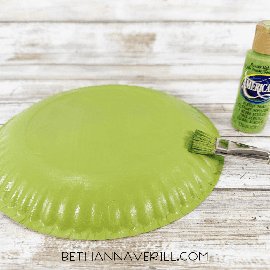 Paper plate painted light green using acrylic paint and a flat paintbrush.