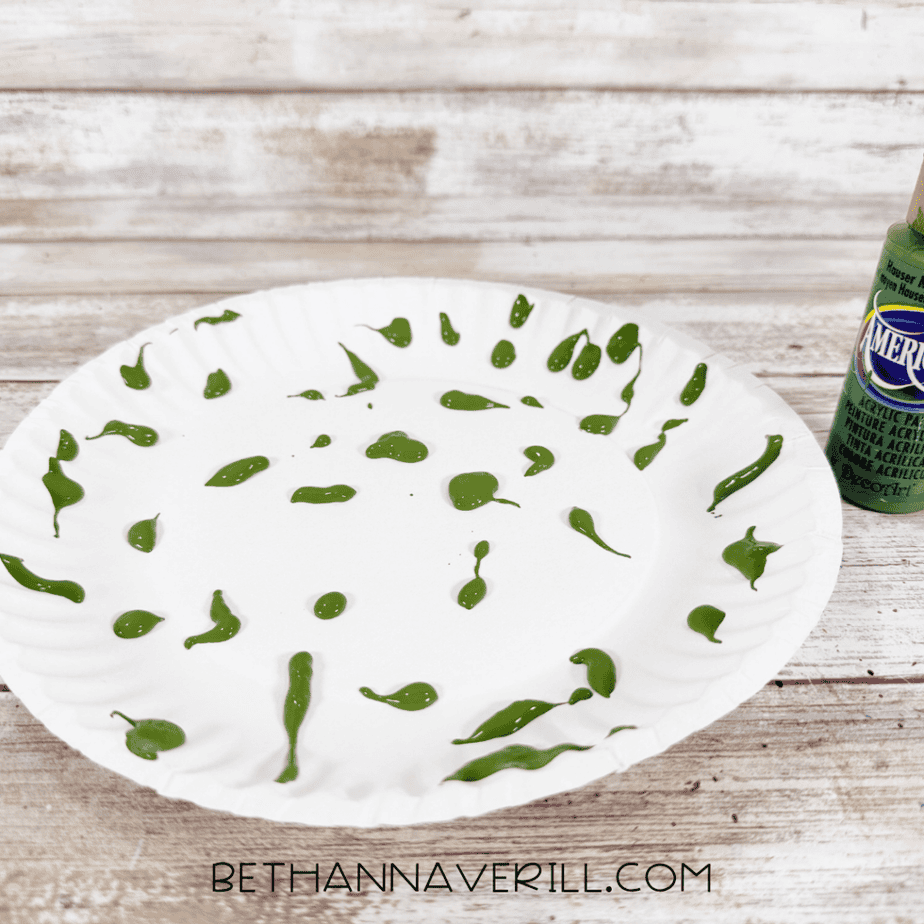 White paper plate dotted with dark green acrylic paint to create a textured tree canopy.