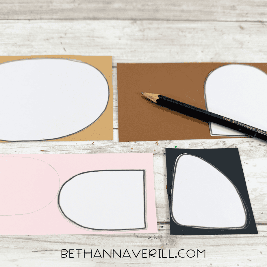 Paper templates traced onto tan, brown, pink, and black paper with a pencil on a white wood surface.