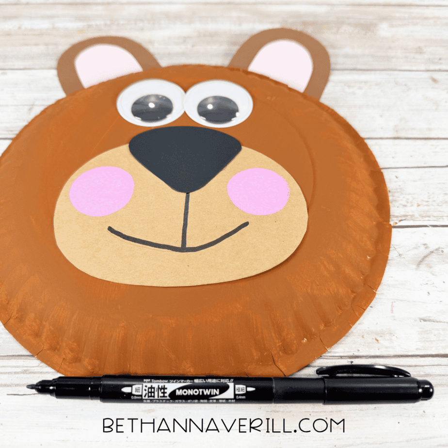 Close-up of a brown paper plate bear face with pink cheeks and a black marker used to draw the mouth.