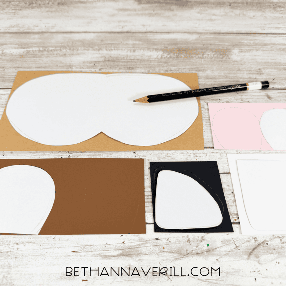 Paper templates being traced onto brown, pink, black, and white paper with a pencil.
