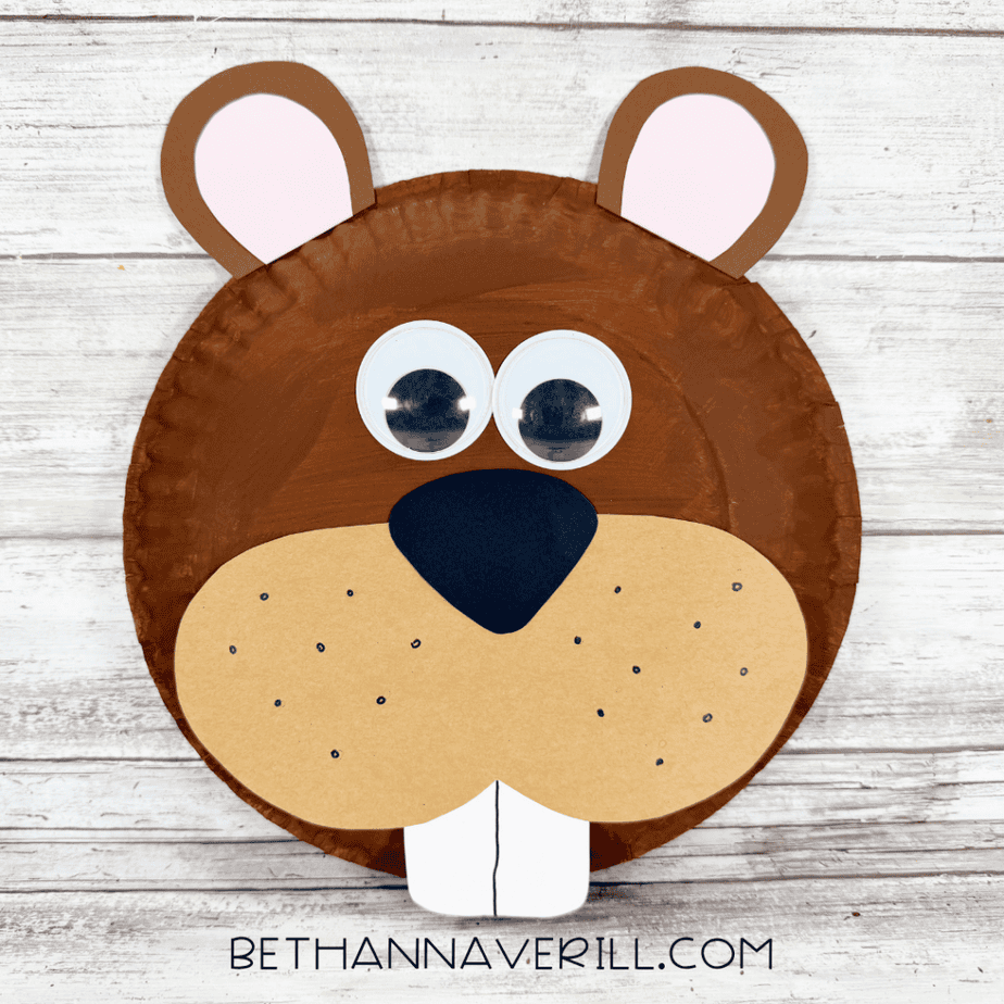 Finished paper plate beaver craft with brown ears, pink inner ears, large googly eyes, tan muzzle, black nose, dotted whisker marks, and two white front teeth.