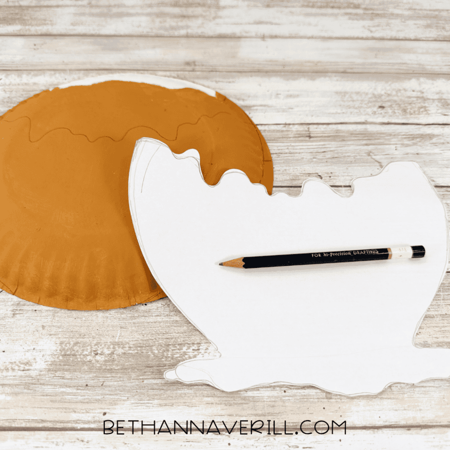 White paper template with a wavy dripping edge beside a caramel brown painted paper plate and pencil.