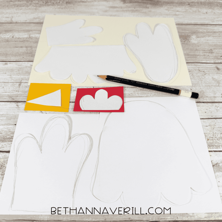 White paper templates traced onto cream, red, yellow, and white paper, with a black pencil resting across the pieces.