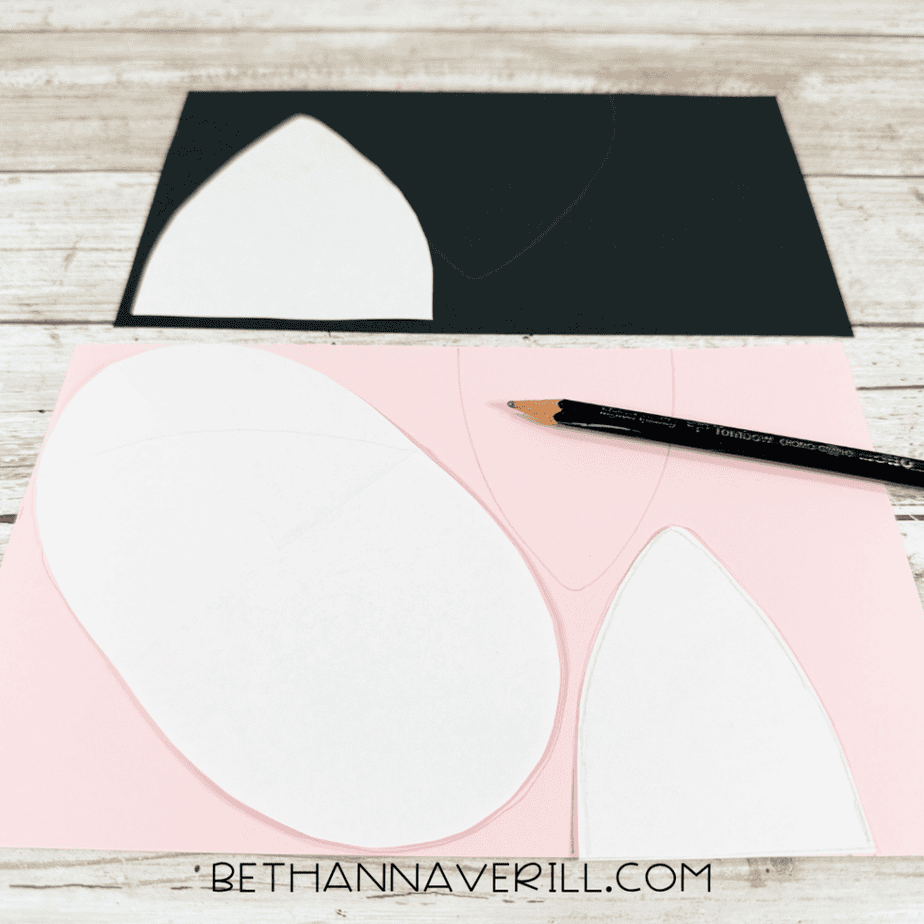 White paper shapes positioned on black and pink paper with traced outlines and a black pencil.