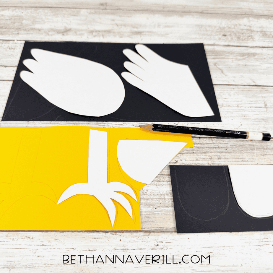 White paper templates placed on black and yellow paper for tracing wing, foot, beak, and other craft pieces.