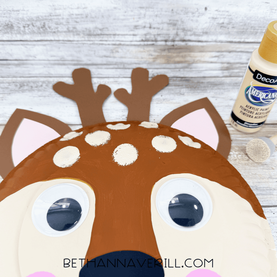 Close-up of a paper plate deer face with cream spots being added to the brown forehead using a sponge brush.