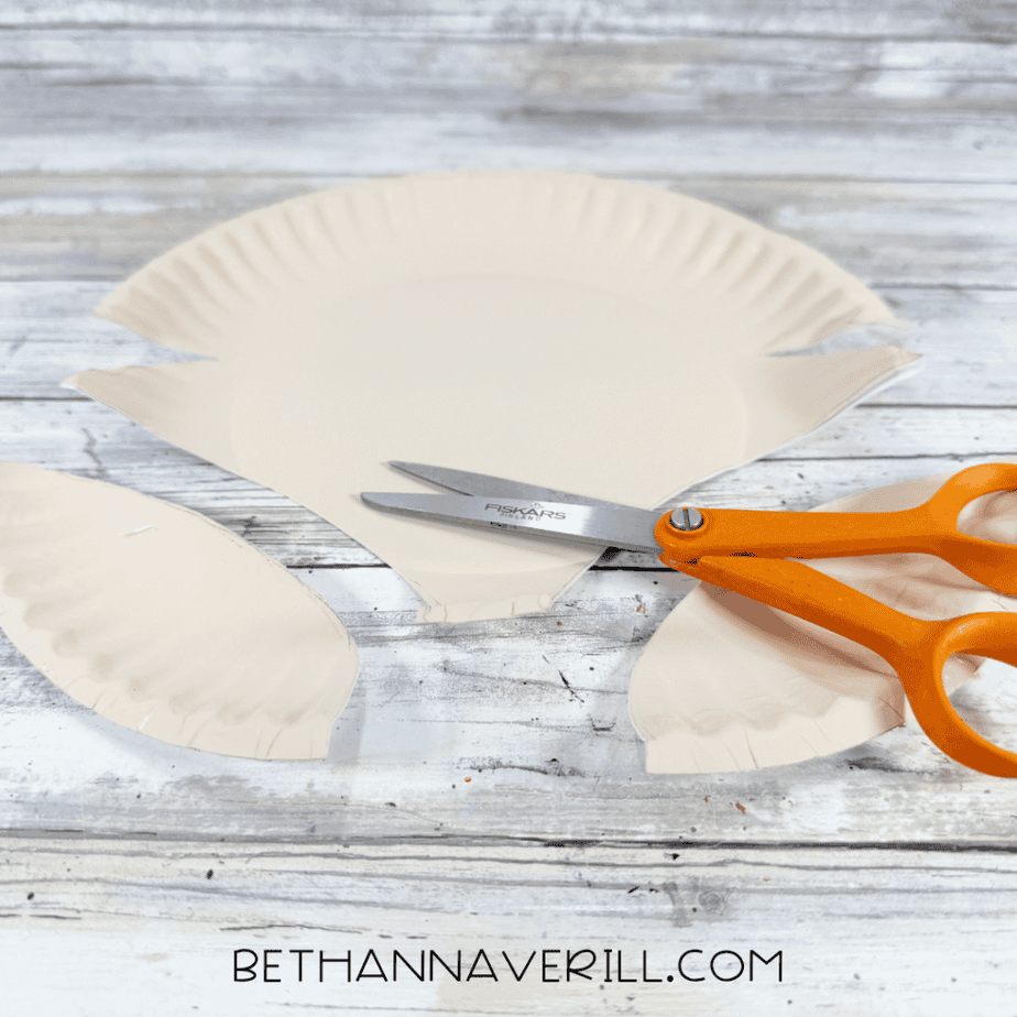 Cream-painted paper plate cut into a pointed fox face shape with curved pieces removed from both sides.