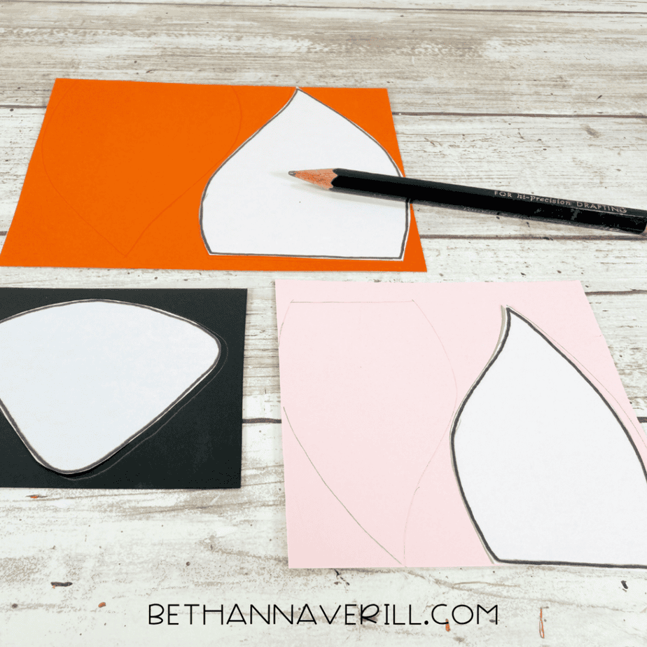 Fox ear and nose templates being traced onto orange, pink and black paper with a pencil.
